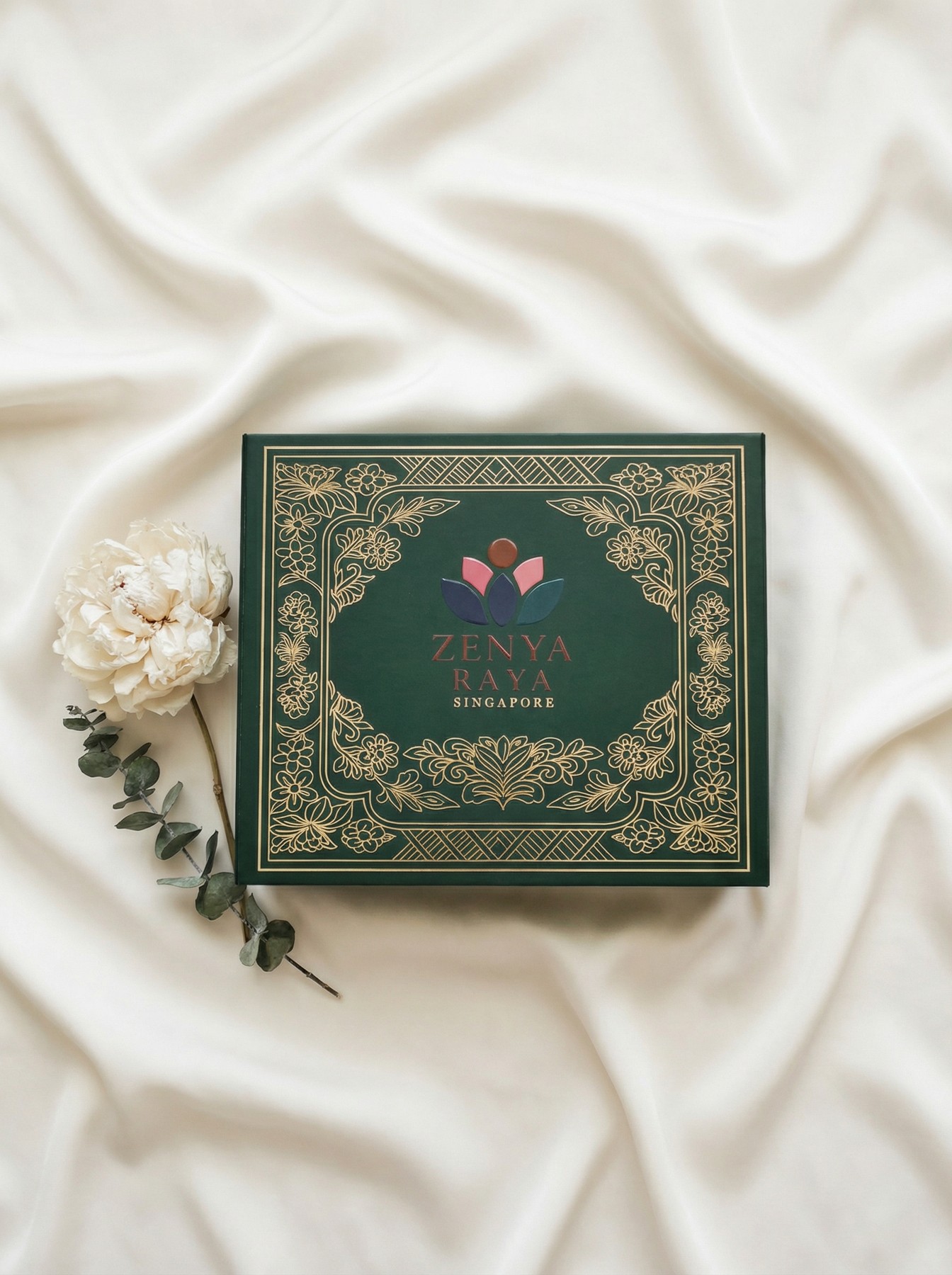A deep-green Zenya Raya box with gold linework, resting on ivory silk